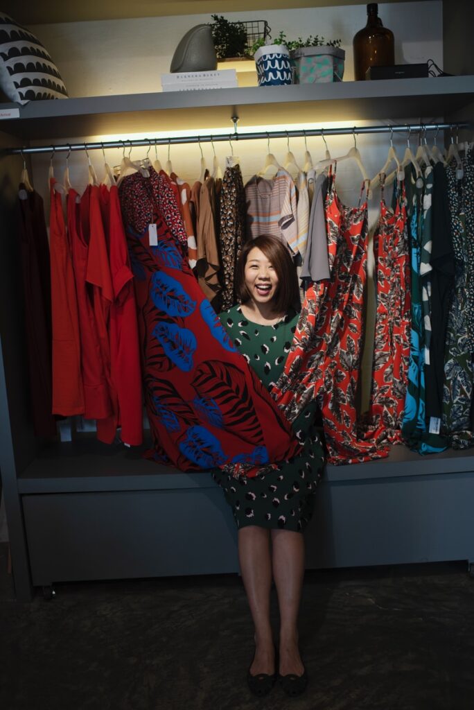 smiling woman standing on different dresses lot